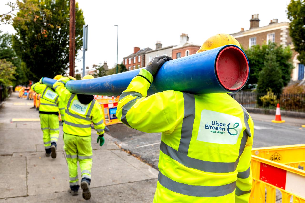 Three Uisce Éireann Engineers carrying a blue pipe in a road work