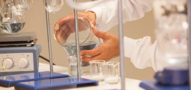 A scientist pouring a liquid into a beaker in a lab