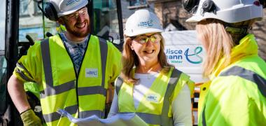 3 Uisce Éireann engineers holding site plans while smiling at eachother