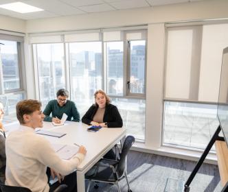 Four graduates sitting on a meeting room desk looking at a television