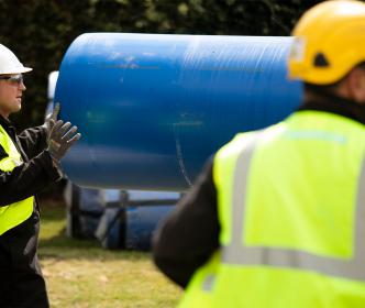 Two engineers holding a large blue pipe wearing safety gears