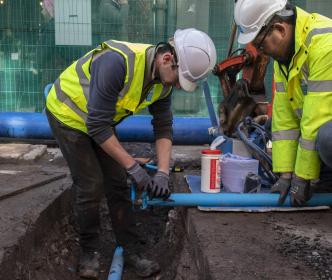 two Uisce Éireann workers laying blue pipes into the ground in a city