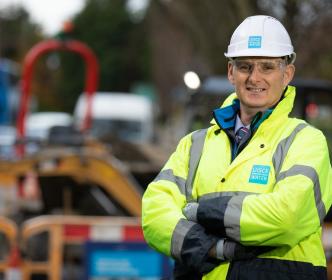 A Uisce Éireann employee wearing a hard hat and hi vis jacket while smiling at the camera