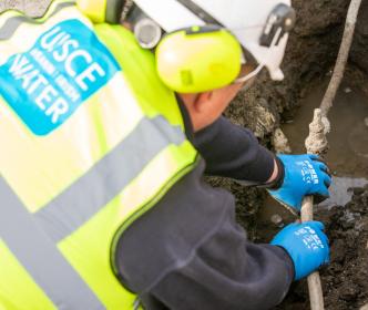 An Uisce Éireann worker fixing a small pipe in the ground