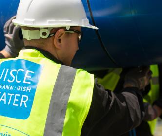 two uisce eirann workers carriny a blue pipe over they're head