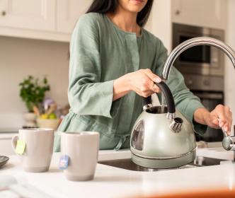 A woman filling a kettle in a kitchen sink