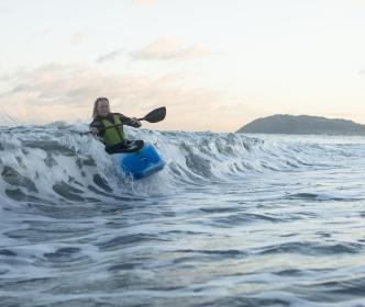 A woman kayaking over a wave in the sea
