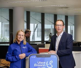 Two people standing next to an oversized phone advertising Uisce Éireann business text alerts