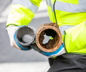 A worker holding a new pipe next to an old and rusty pipe