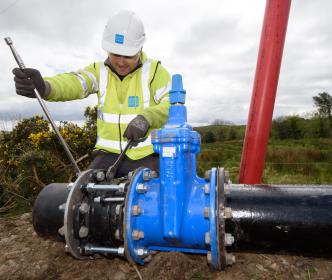 Uisce Éireann worker repairing damaged pipes with a wrench and lever 