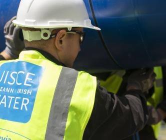 a Uisce Éireann worker caring a blue pipe over his head 