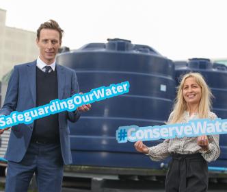 A man holding a sign reading "#SafeguardingOurWater" and a woman holding a sign reading "#ConserveWater"