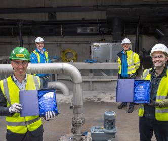 Four workers in hi-vis jackets and hard hats, with two holding glass trophies and smiling