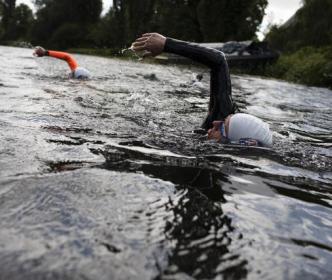 Two swimmers in wetsuits swimming in a river