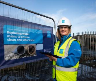 An Uisce Éireann worker in front of a Leakage Reduction Programme sign