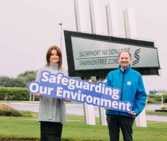 A man and a woman holding a sign reading "Safeguarding our environment" in front of a wave backdrop