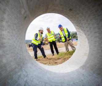 Three men in hi-vis jackets and hard hats looking into a large pipe