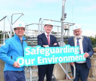 Three men holding a sign that reads "Safeguarding Our Environment" at a water treatment plant