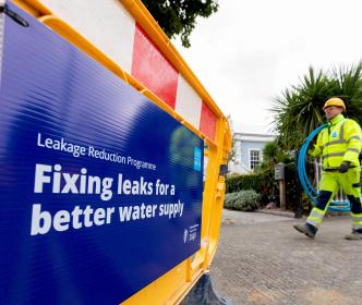 An Uisce Éireann worker carry some blue piping on a site with a sign reading "Fixing leaks for a better water supply"