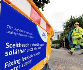 An Uisce Éireann worker carrying blue piping on a site