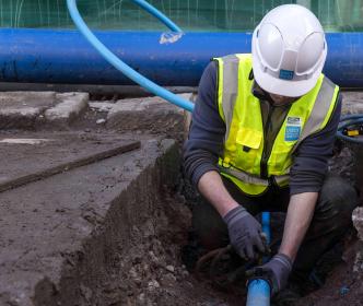 An Uisce Éireann worker fixing a blue pipe in the ground