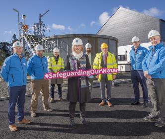 A group of people in hard hats, with one woman holding a sign reading "#SafeguardingOurWater"