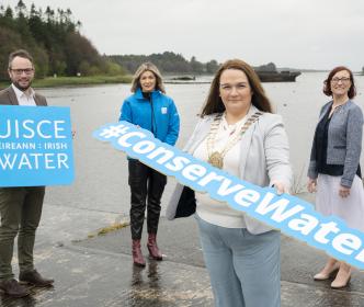 A group of people with a woman holding a sign reading "#ConserveWater"