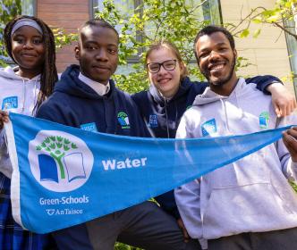 Four schoolchildren holding a Green-Schools water flag