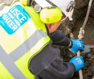 An Uisce Éireann worker fixing a small pipe in the ground