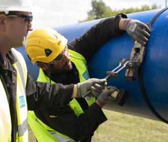 Two Uisce Éireann workers working on a large blue pipe